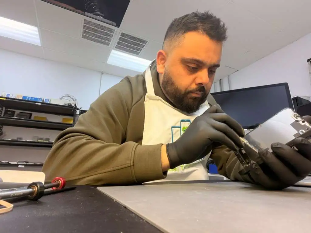 Cracked iPhone screen next to repair tools on a workbench